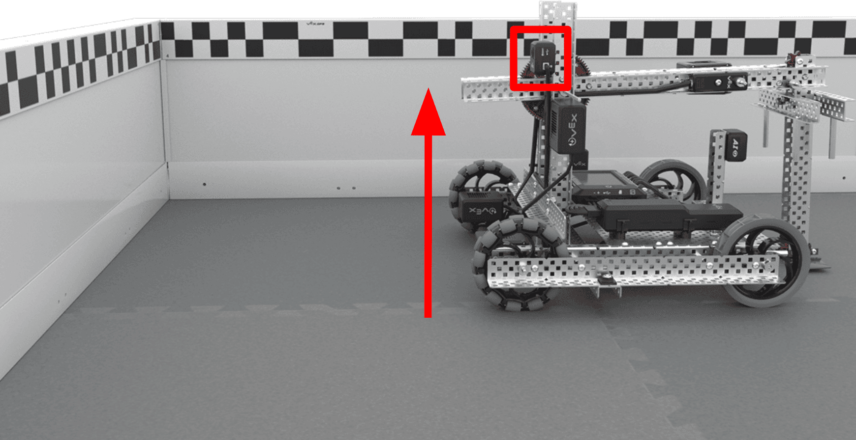 Axel, the Hero Bot for the 2024-2025 High Stakes game, on an empty Field in the corner, with the GPS Sensor mounted to the rear of the robot facing the Field Code on the perimeter of the Field. There is a red box highlighting the GPS Sensor position on the robot and and arrow illustrating the height of the sensor at the same height as the Field Code.
