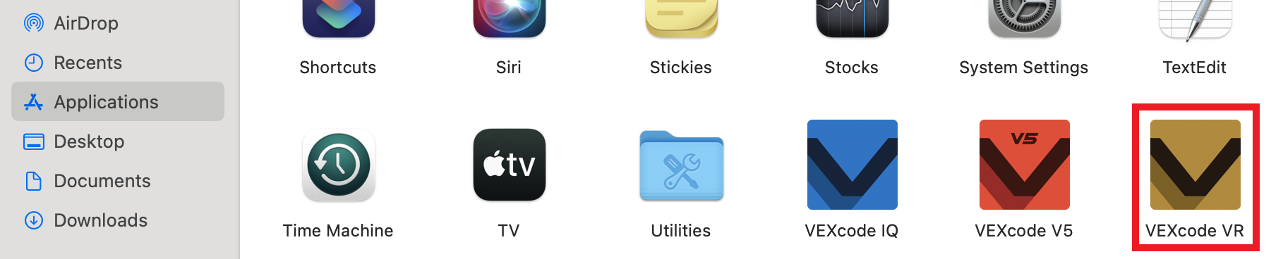 MacOS:n Sovellukset-kansioikkunassa näkyy erilaisia ​​sovelluskuvakkeita, mukaan lukien VEXcode VR, korostettuna punaisella ääriviivalla. Muita näkyviä sovelluksia ovat VEXcode IQ, VEXcode V5, järjestelmäasetukset, TextEdit, Stickies, Stocks, TV ja Time Machine. Vasemmalla oleva sivupalkki näyttää navigointivaihtoehdot, kuten AirDrop, Viimeisimmät, Sovellukset, Työpöytä, Asiakirjat ja Lataukset. VEXcode VR -kuvake on sijoitettu kansion näkyvän osan oikeaan alakulmaan.
