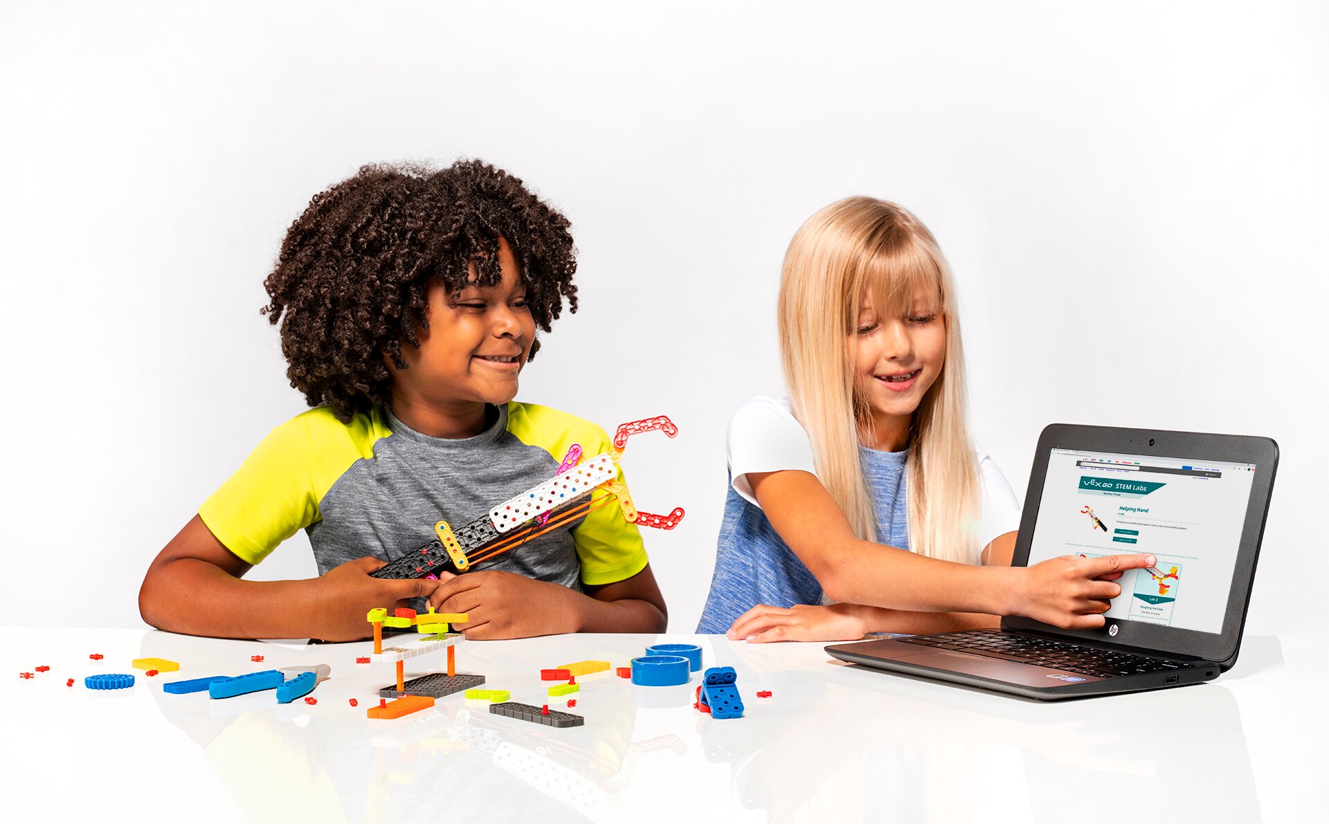 Two students collaborating in a classroom environment using VEX GO pieces and a computer.