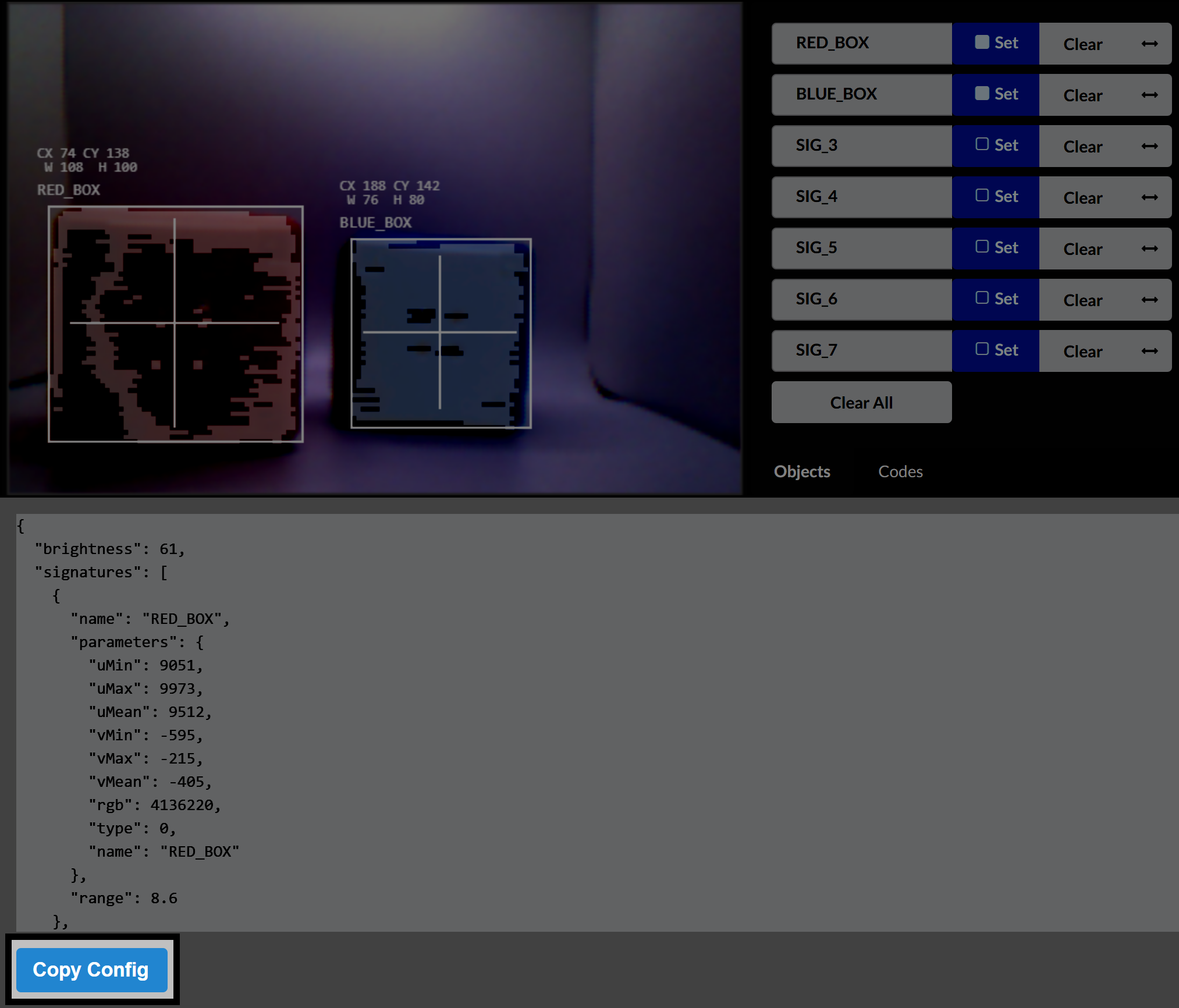 The Vision Sensor utility interface shows a live preview with two objects detected and labeled as RED_BOX and BLUE_BOX. Their bounding boxes are displayed with crosshairs, and coordinate data is shown for each. Below the preview, a JSON configuration snippet for RED_BOX is visible, including brightness, signature name, and color parameters. A blue button labeled Copy Config is highlighted at the bottom.