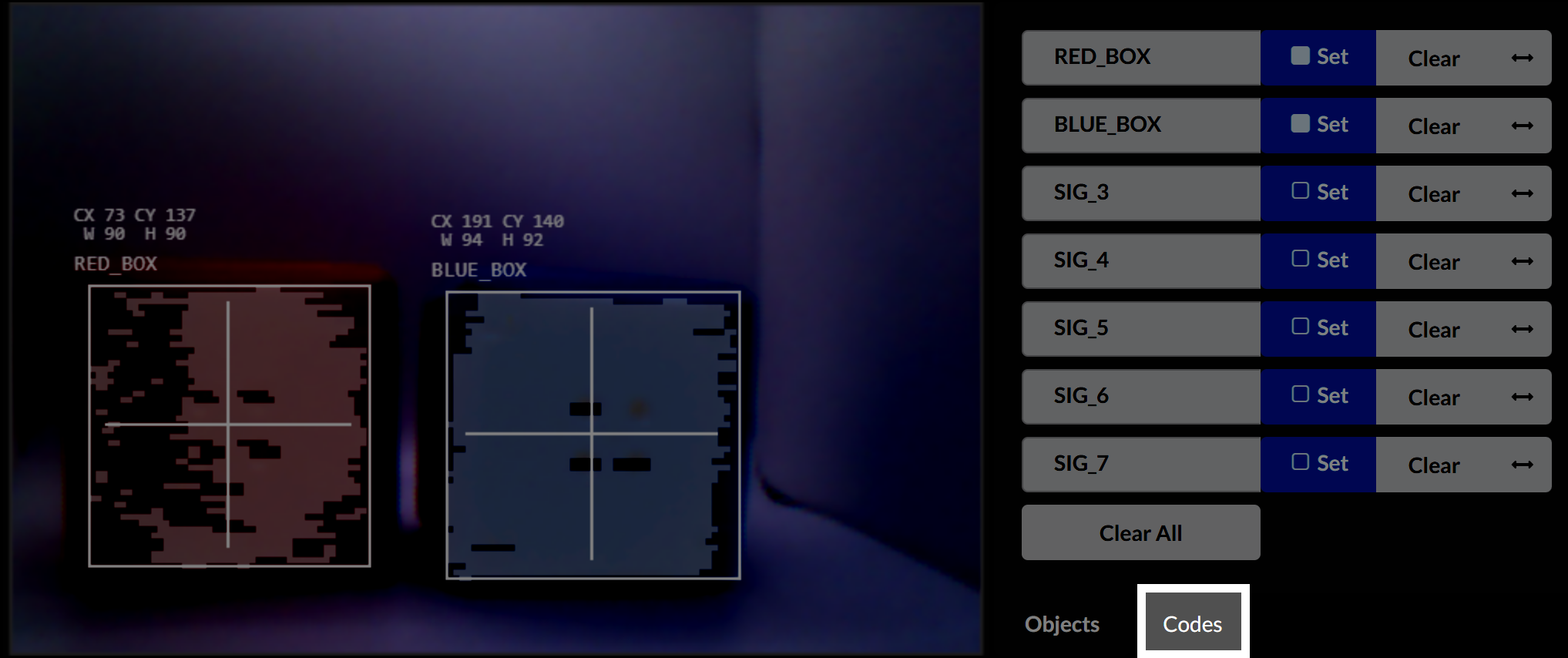 The Vision Sensor preview shows two tracked objects labeled RED_BOX and BLUE_BOX, each with a bounding box and crosshair overlay. The red box is on the left with coordinates CX 73, CY 137, width 90, and height 90. The blue box is on the right with coordinates CX 191, CY 140, width 94, and height 92. On the right side, the signature list includes RED_BOX and BLUE_BOX. The Codes tab at the bottom is highlighted.