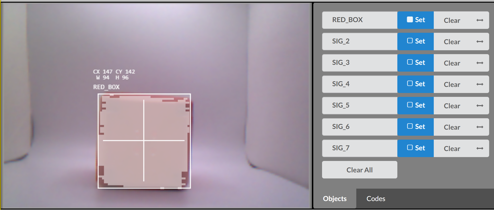 The Vision Sensor preview showing a red cube being tracked. A white bounding box and crosshair overlay surround the object, labeled RED_BOX. The coordinates CX 147, CY 142, width 94, and height 96 are displayed in white text above the object. On the right, the RED_BOX signature is listed and selected among other SIG entries.