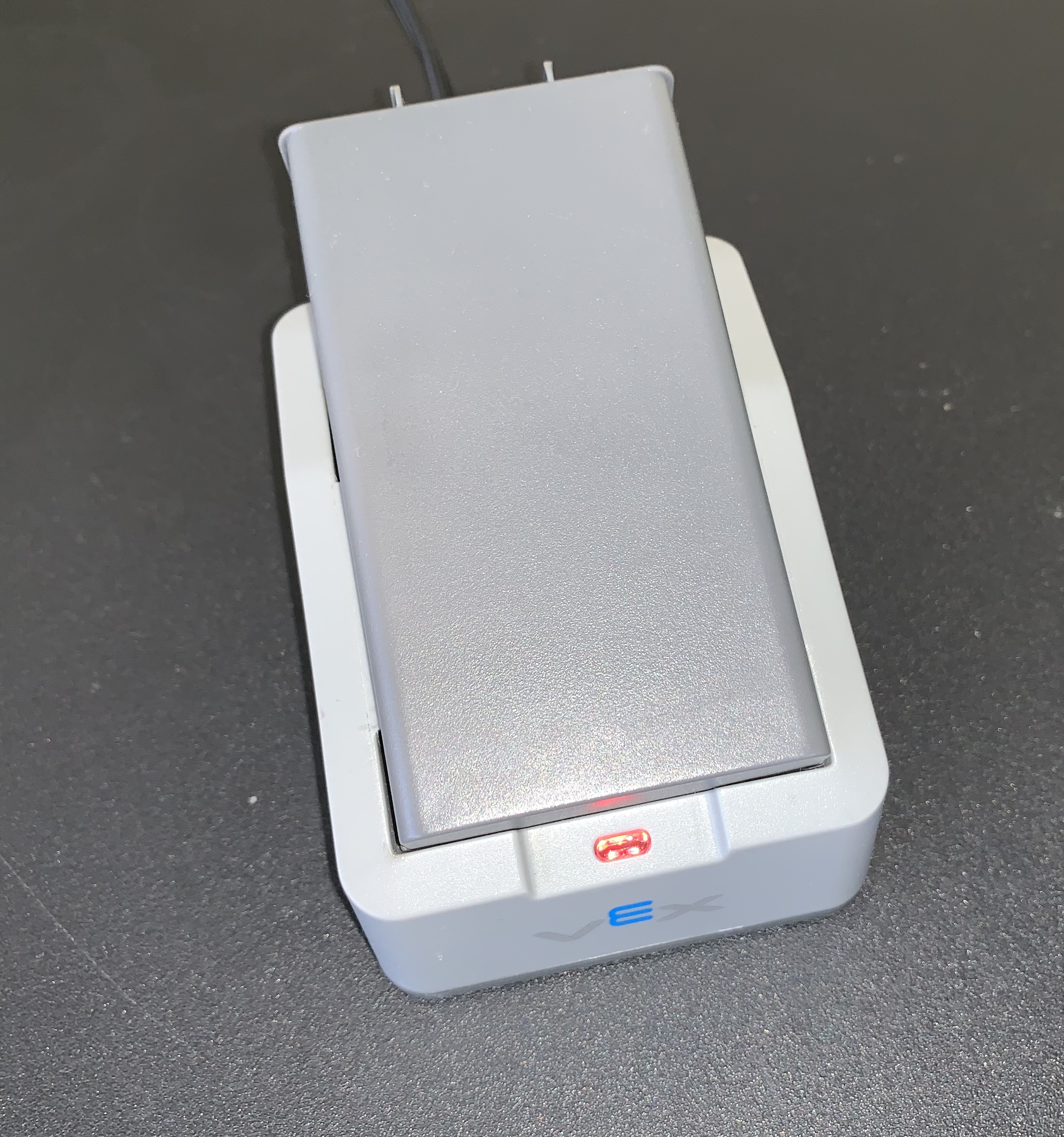 Die Roboterbatterie wurde in das Ladegerät eingesetzt. Das Ladegerät wird über das Netzkabel an eine Stromquelle angeschlossen und verfügt über eine rote Kontrollleuchte.