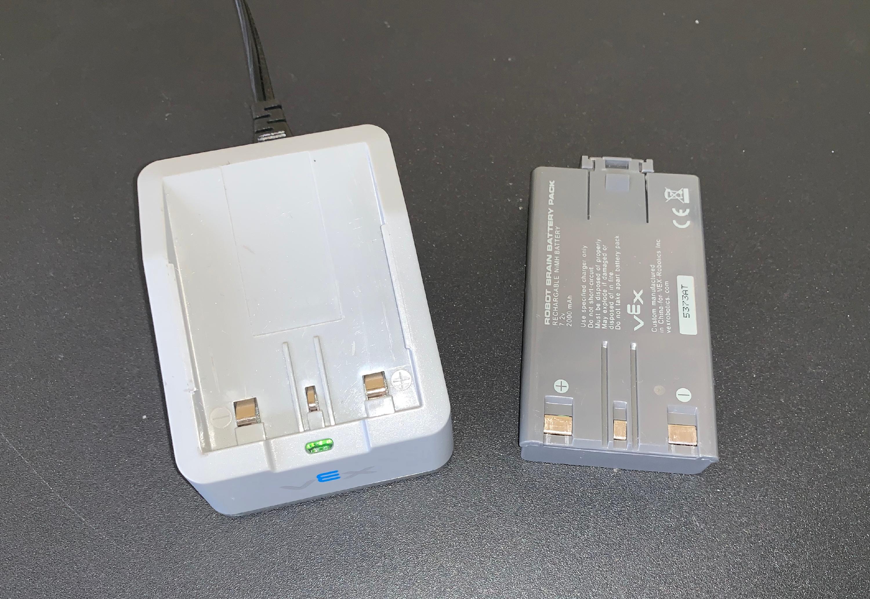 Une batterie de robot et un chargeur de batterie de robot placés ensemble sur une table. Le chargeur est connecté à une source d'alimentation à l'aide de son cordon d'alimentation.