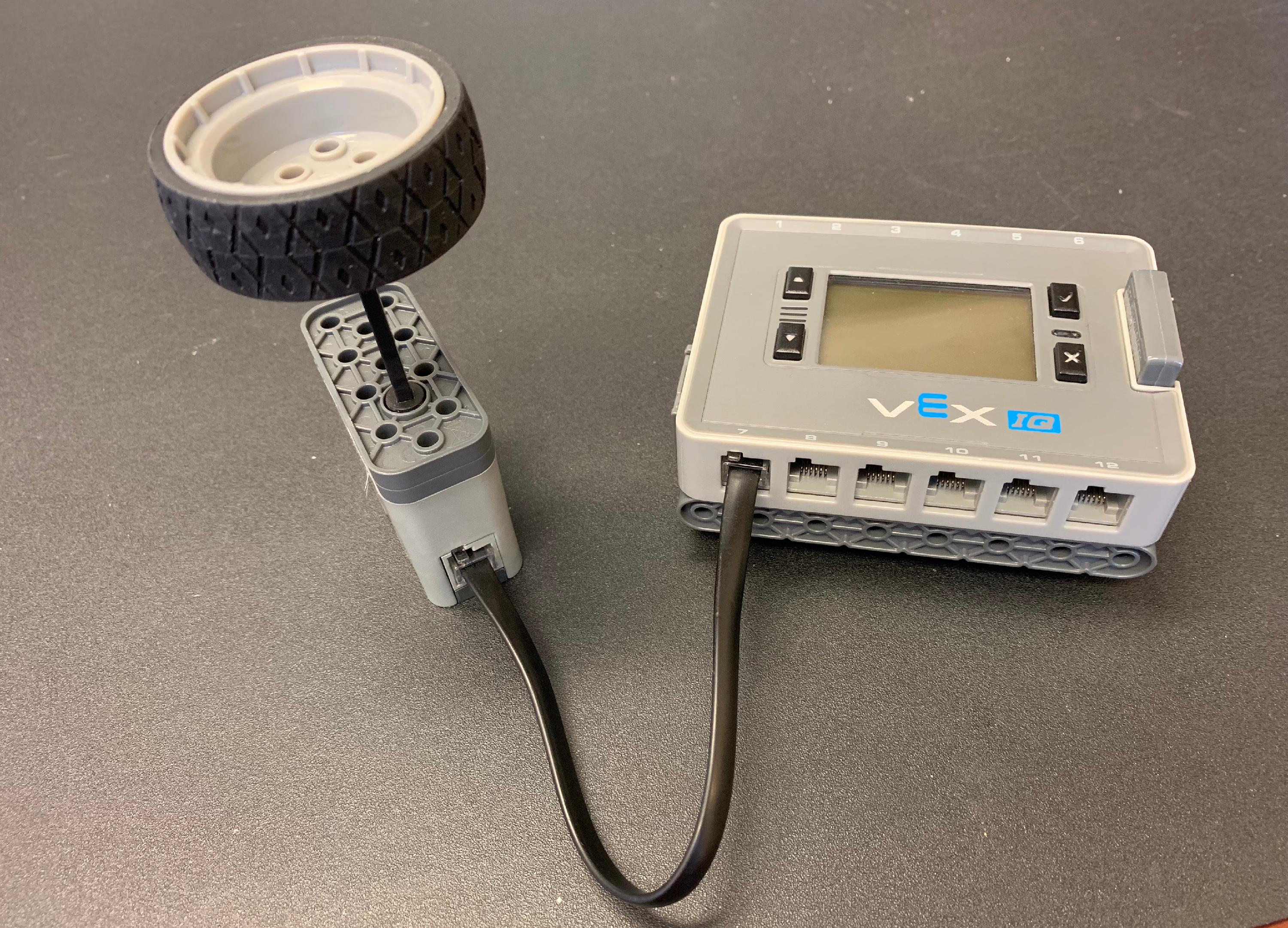 Un cervello con QI e batteria è posizionato su un tavolo. Uno Smart Motor è collegato a una delle sue Smart Port. Un albero motore attaccato a un pezzo di ruota è collegato al motore intelligente, in modo che quando la ruota gira, anche il motore intelligente gira.