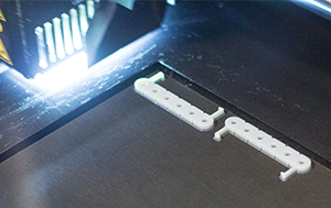 Individuell gefertigte, 3D-gedruckte Handyhalterungsteile, die mit VEX IQ kompatibel sind. Die Druckteile sind gerade fertig und liegen noch auf dem Drucker.