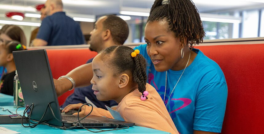 Mokytojas įtraukia mokinį į VEX IQ pamoką nešiojamuoju kompiuteriu.