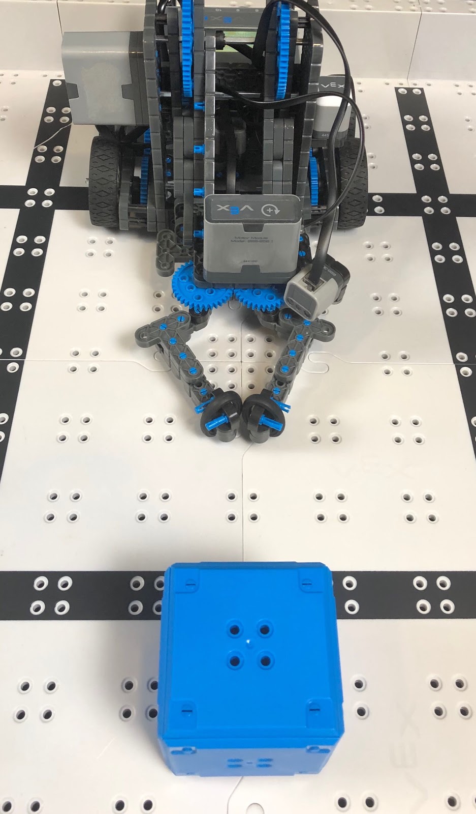 VEXcode IQ Clawbot na polu IQ z umieszczoną przed nim niebieską kostką.