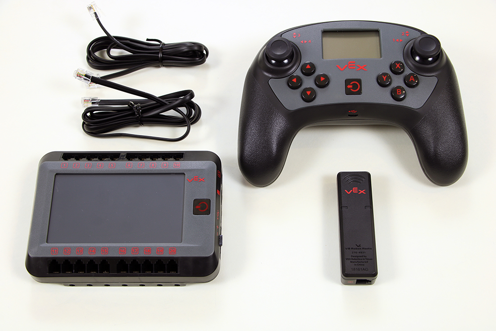 Espacio de trabajo con todos los elementos necesarios para emparejar el controlador con el cerebro. Las piezas incluyen un cerebro robótico V5 alimentado, un controlador V5, una radio robótica V5 y dos cables inteligentes.