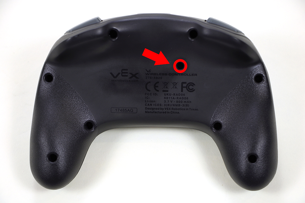 V5 コントローラーの背面には、特定の穴が強調表示され、矢印で示されています。 リセット ボタンの穴は、コントローラーの背面の中央近く、仕様ラベルのすぐ上にあります。