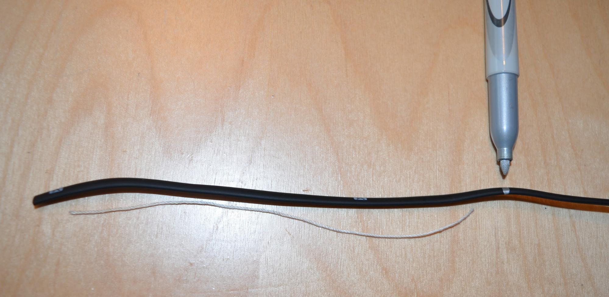 Een afgeknipt stuk touw wordt naast een stuk kabel gelegd en met een markeerstift wordt de afmeting van het touw op de kabel zelf overgebracht. Aan beide kanten is ongeveer 1,5 cm ruimte gelaten voor de aansluitingen.