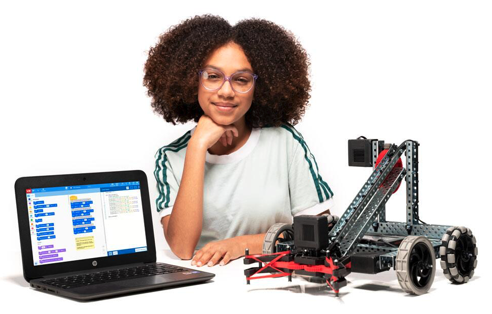 Mokinys sėdi prie „V5 Clawbot“ roboto ir nešiojamojo kompiuterio, kurio ekrane rodomas „VEXcode V5 Blocks“ projektas.