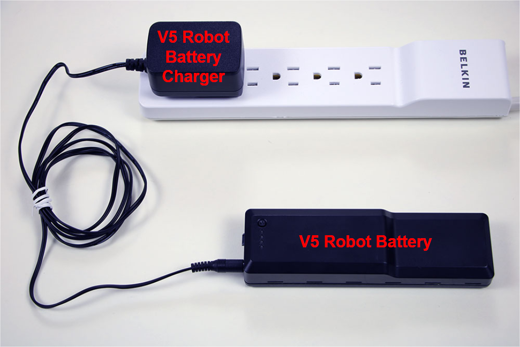 La batterie du robot V5 est représentée en charge à l'aide du chargeur de batterie du robot V5, lui-même connecté à une prise de courant sur une multiprise.