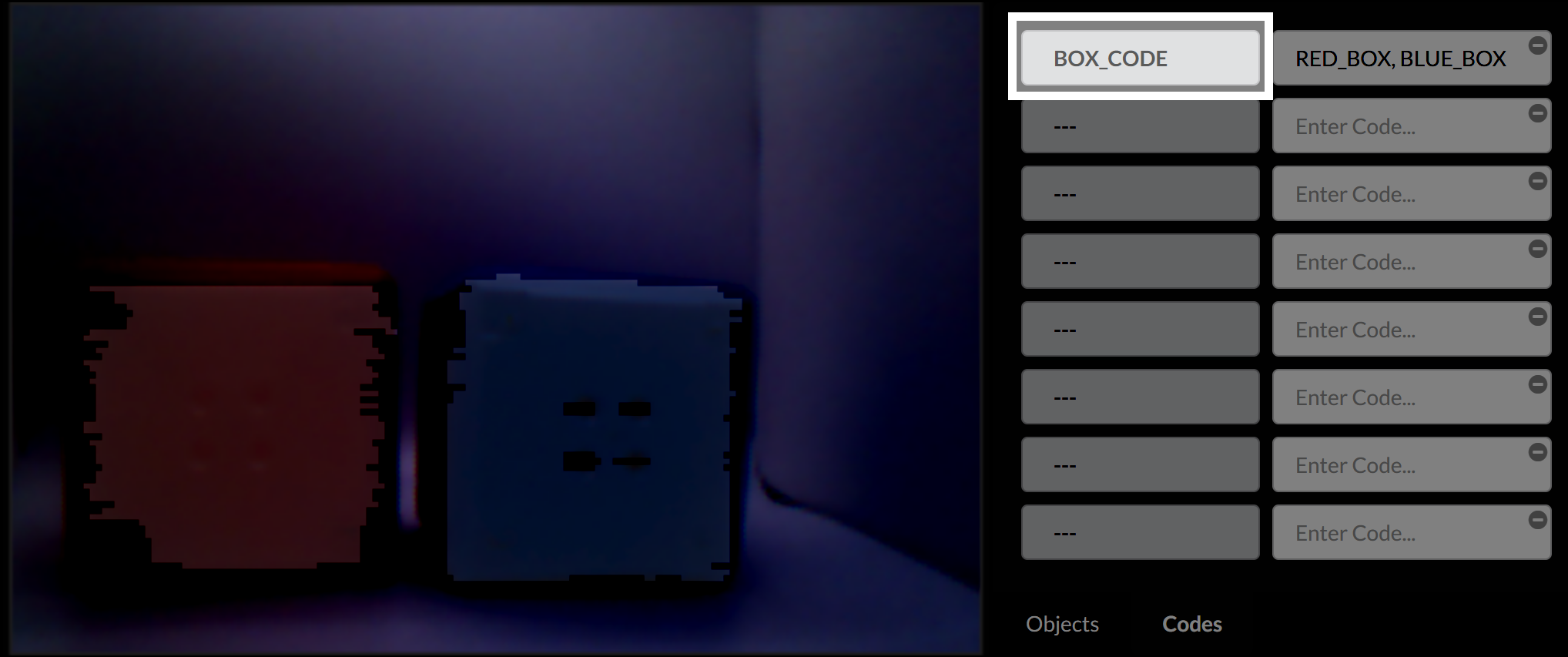 A Vision Sensor előnézete ismét egymás mellett mutatja a piros és kék kockákat. Egy egyéni címke, a BOX_CODE, a kódlista jobb felső sarkában látható, amely a RED_BOX és a BLUE_BOX elemeket egy bejegyzés alá csoportosítja. A csoportosított bejegyzés a kockanevekkel megegyező sorban jelenik meg.