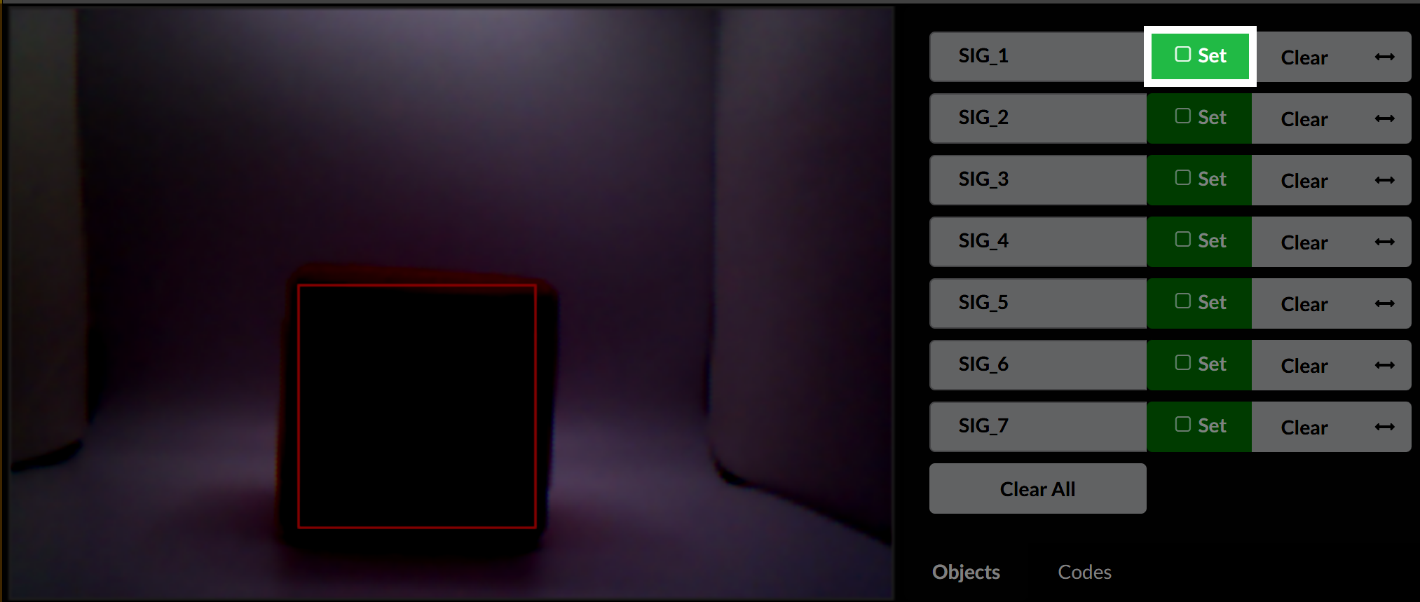 Vista previa del sensor de visión con un cubo rojo delineado en un cuadro de detección rojo. El brillo es bajo y la imagen es oscura. En el lado derecho, la ranura SIG_1 tiene su botón Establecer resaltado, lo que indica que está activo para el entrenamiento de firma.