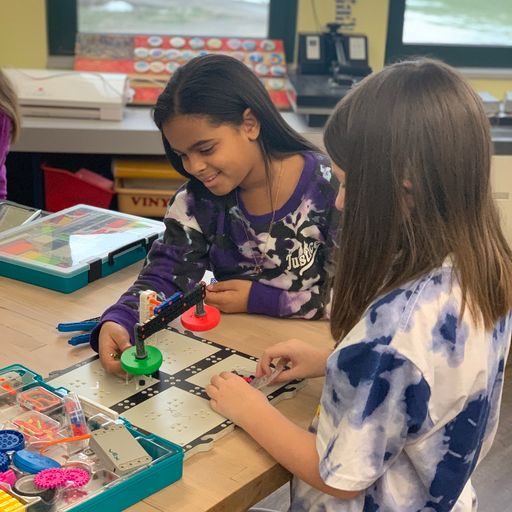 Two female students work together to build the VEX GO Lever in a classroom.