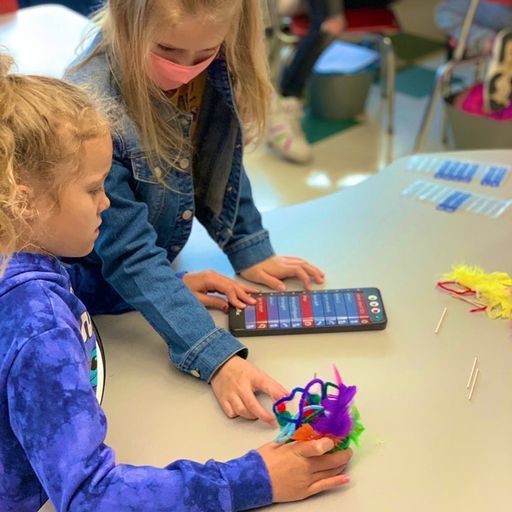 Two female students sit with a decorated 123 Robot on a table, as they edit the Coder card project in their Coder.