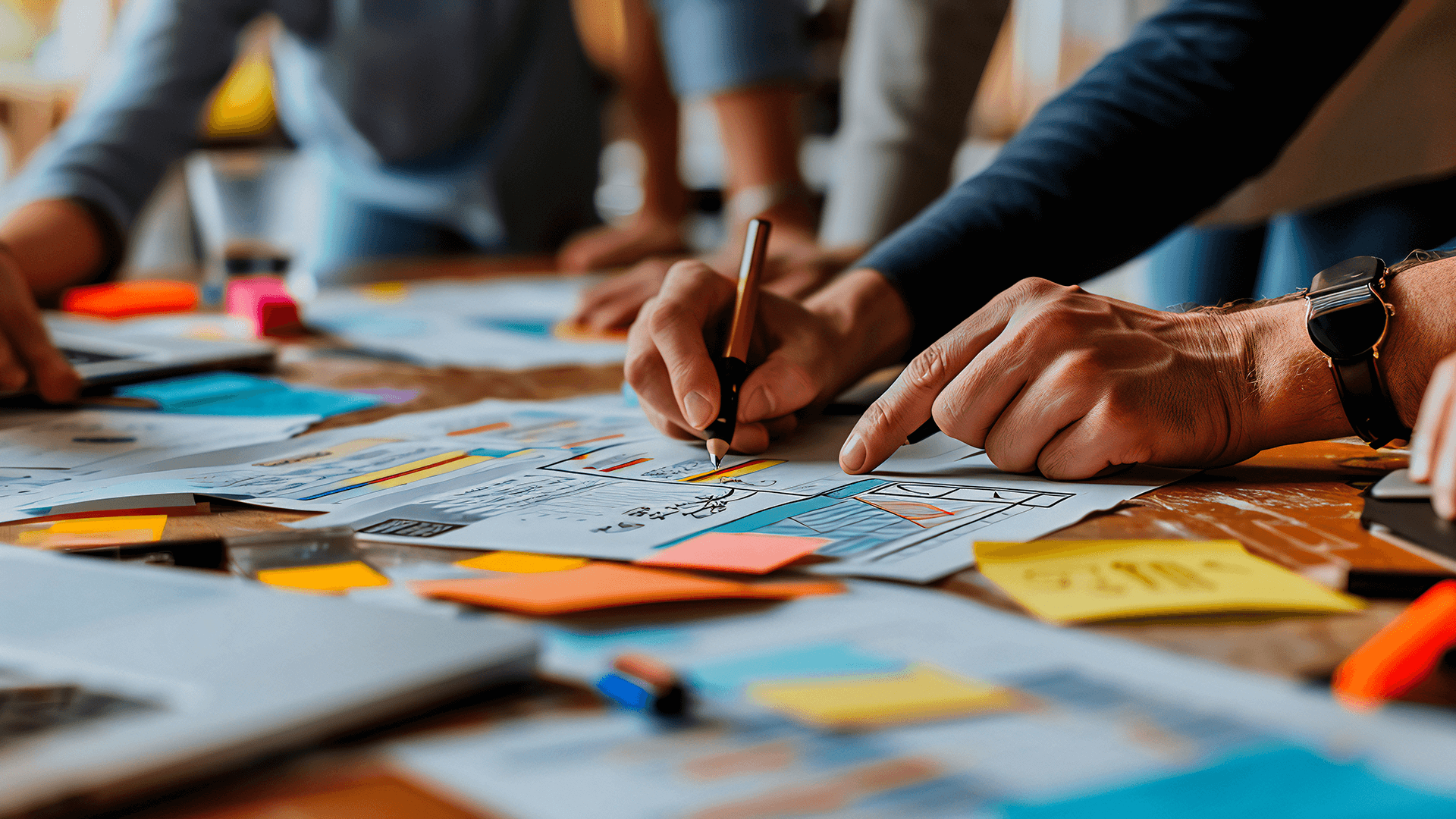 A close up of a table with many sticky notes and diagrams, showing hands writing on a note paper with other people around the table.