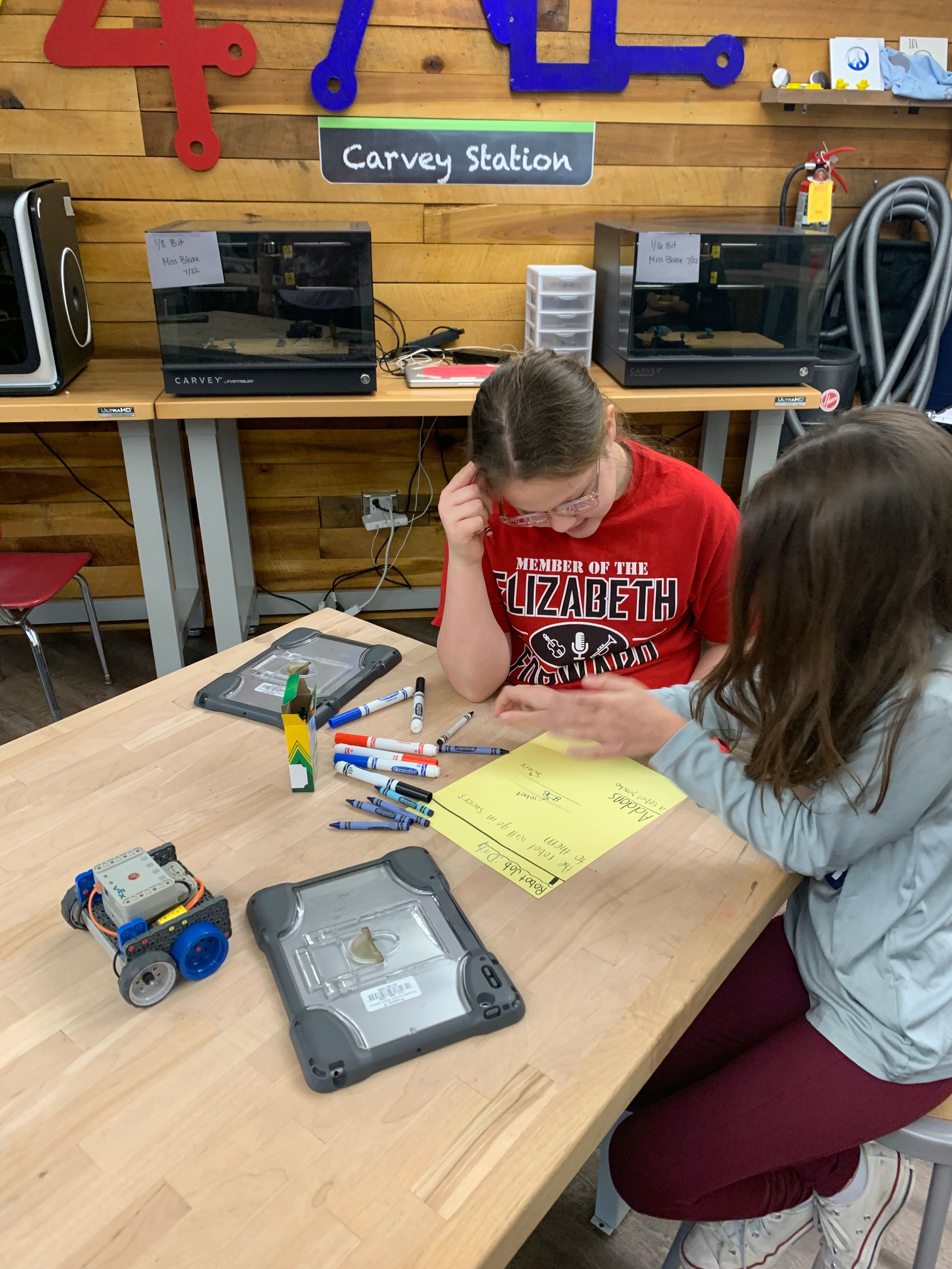 Two female students taking notes about their build and project with a VEX GO Code Base sitting beside them on the table.