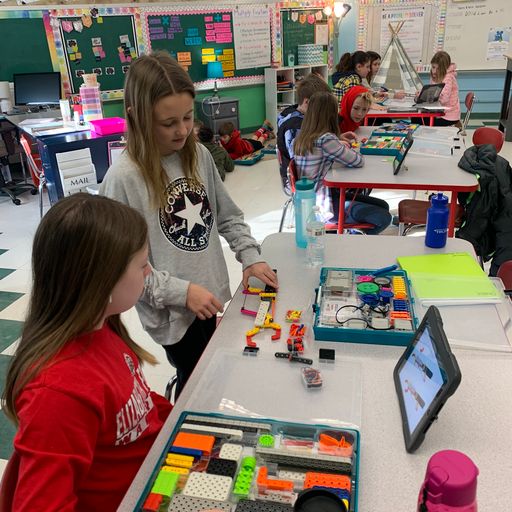 Several student groups work at tables in a classroom to build with VEX GO.