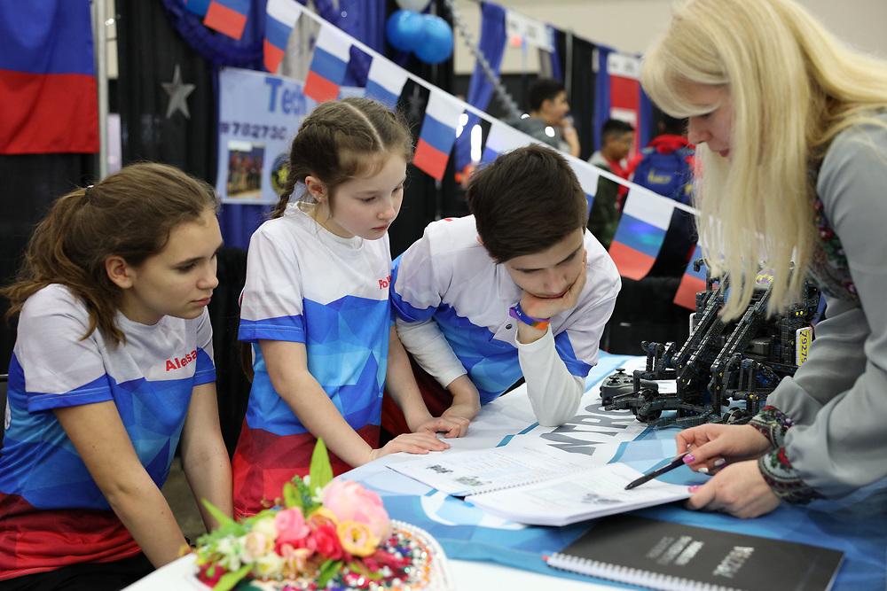 Three students at a competition discussing their engineering notebook with an adult