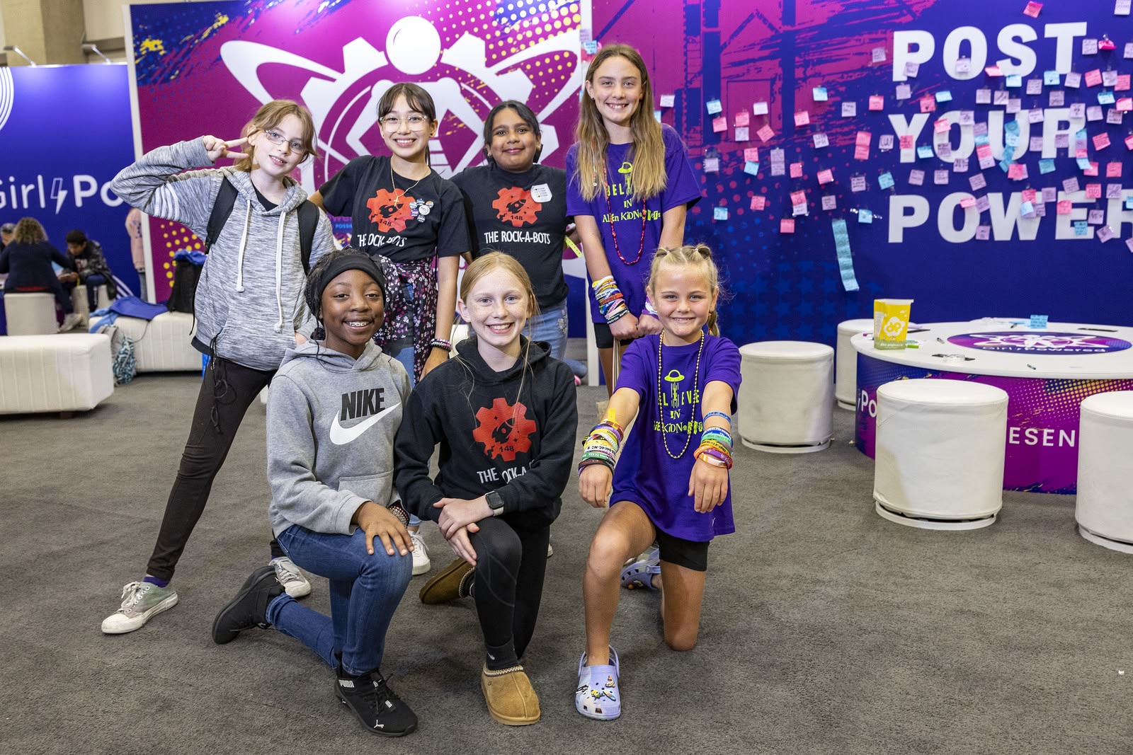 Seven girls in robotics team t-shirts pose in the Girl Powered booth at the VEX World Championships.