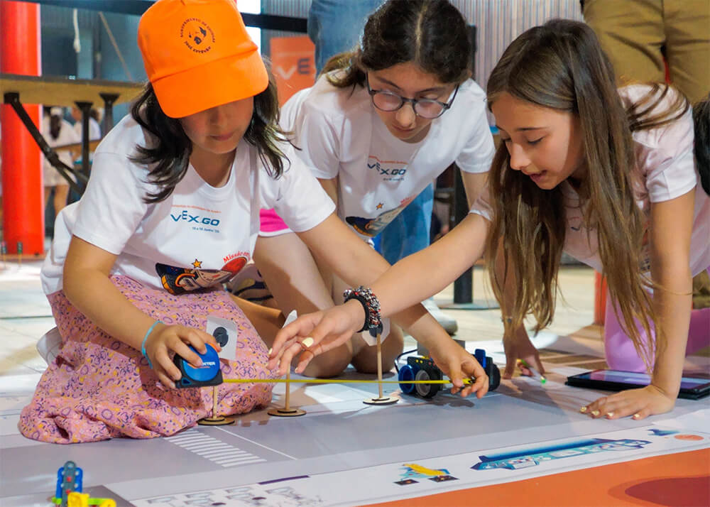 Three girls work together to measure a distance on the floor as they code their VEX GO robot.