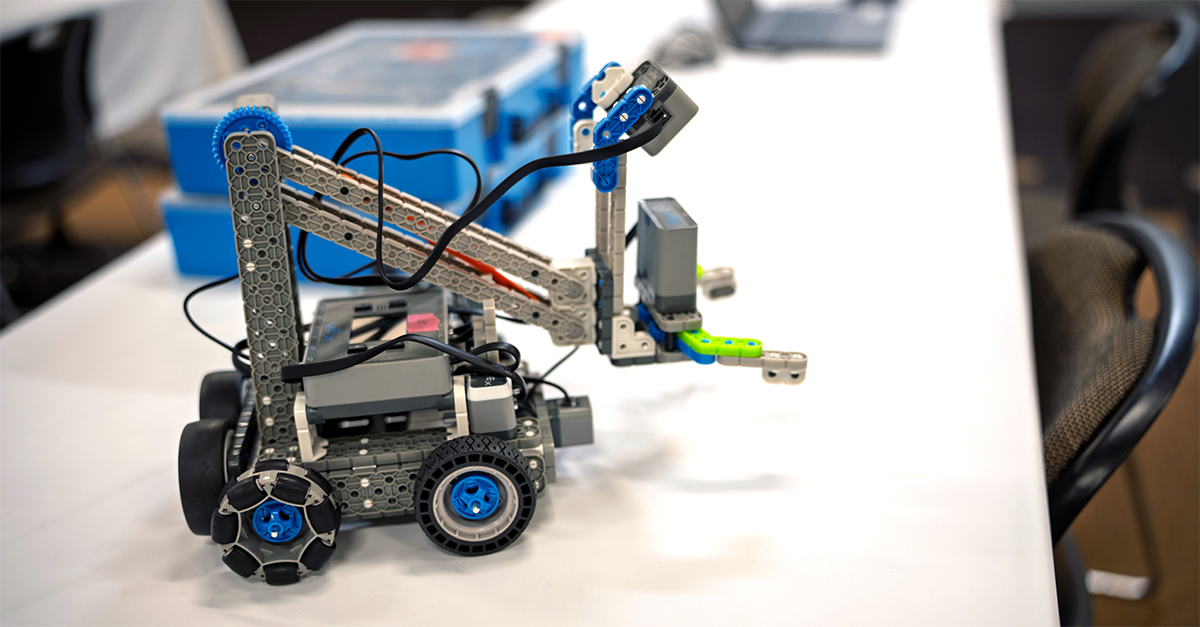 Ένα μόνο VEX IQ Clawbot σε ένα τραπέζι με δύο στοιβαγμένα κιτ VEX IQ στο φόντο.
