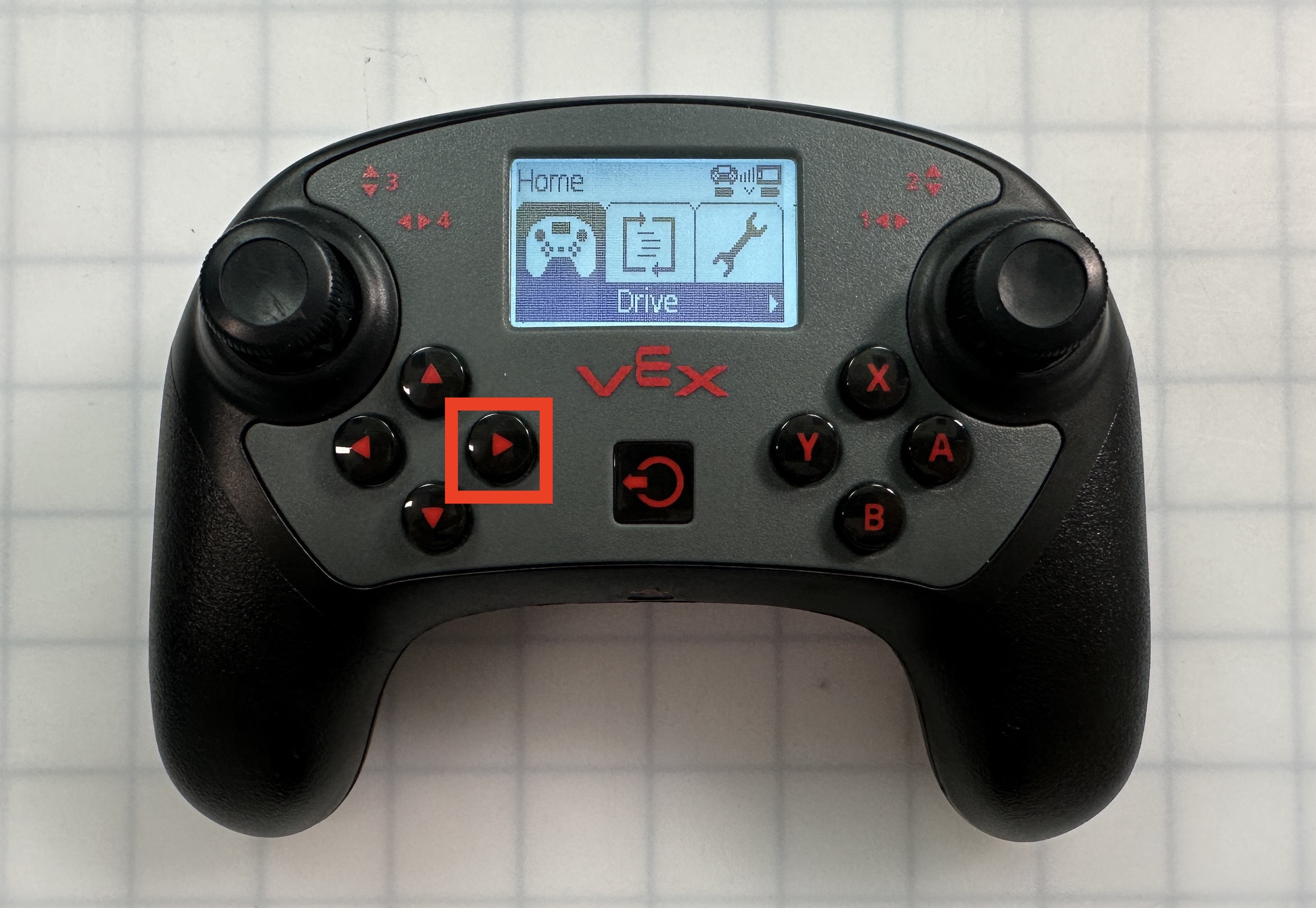 La manette V5 est affichée avec le menu Accueil ouvert et le bouton flèche droite mis en surbrillance.